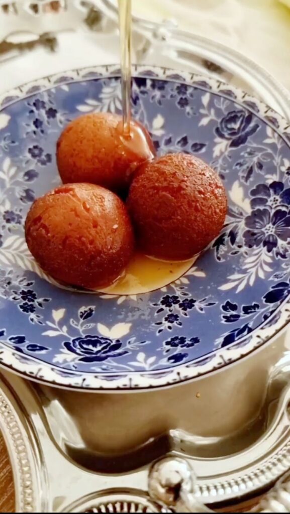 Pouring warm syrup over freshly fried gulab jamuns