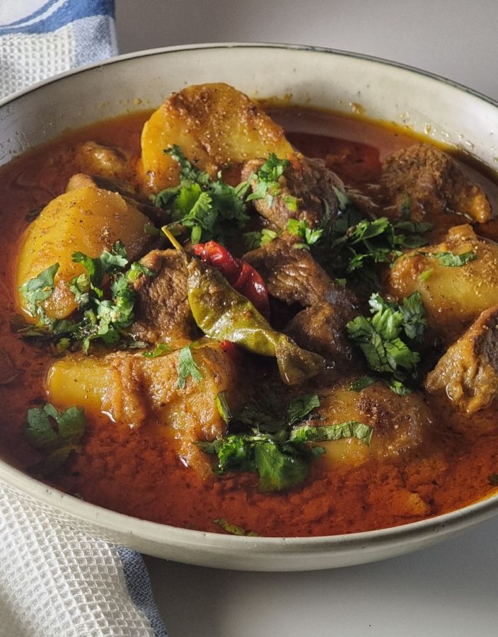 Side view of meat and potato curry with rich masala sauce