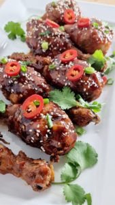 Crispy fried sweet chilli chicken drumsticks coated in sticky sweet and sour sauce, garnished with sesame seeds and fresh spring onions