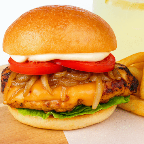 Closeup grilled chicken burger with melted cheese, caramelised onions, and salad leaves in a toasted bun