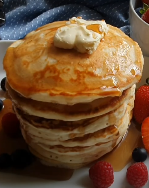 Maple syrup dripping down stack of freshly cooked fluffy pancakes