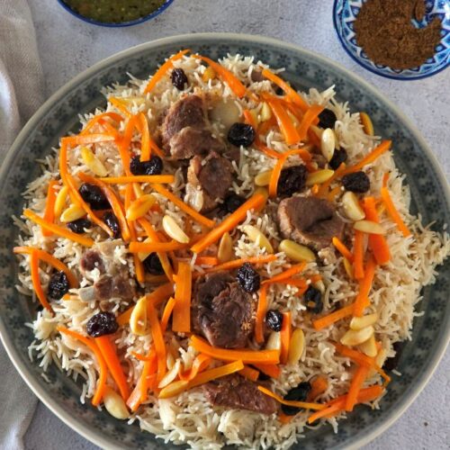 Authentic Afghani Pulao served on a large platter, topped with tender lamb pieces, caramelised carrots, raisins, and almond