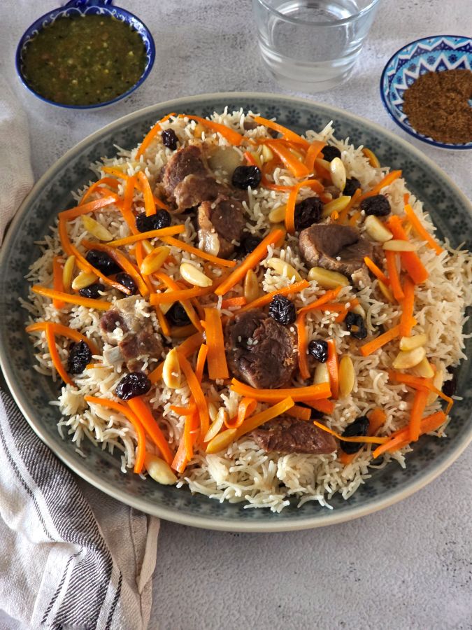 Afghan Pulao garnished with carrots, raisins, and nuts and tomato chutney on side