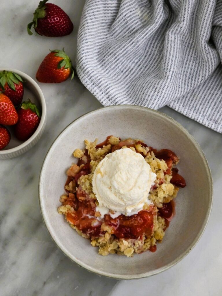 Serving of warm strawberry crumble in a bowlwith vanilla ice cream
