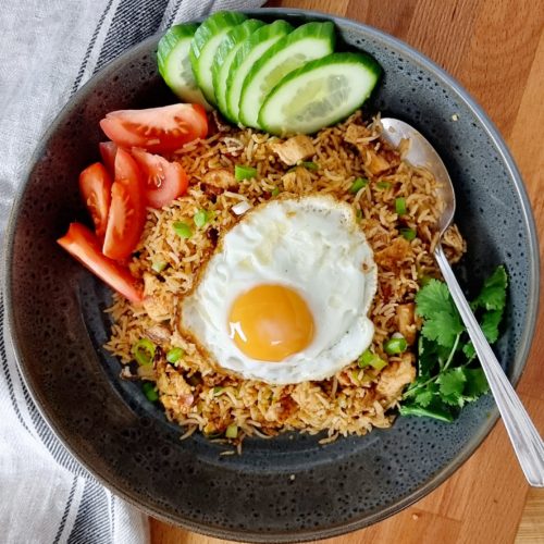 Nasi goreng served with eggs tomatoes and cucumbers