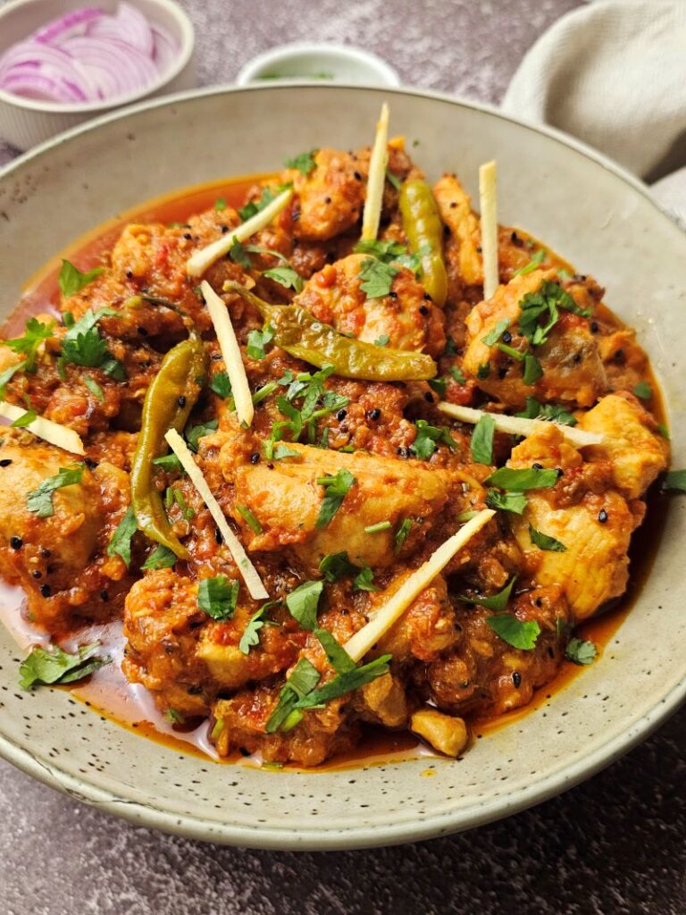 Spicy and tangy Achari chicken in a bowl garnished with ginger and cilantro