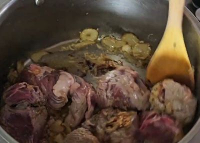 Beef pieces being added to a pot with sautéed onions for Nihari