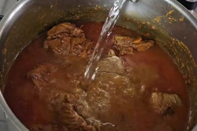 Pouring water into the Beef Nihari pot before slow cooking