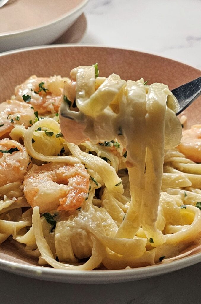 creamy garlic prawn pasta in a plate wrapped around on a fork.