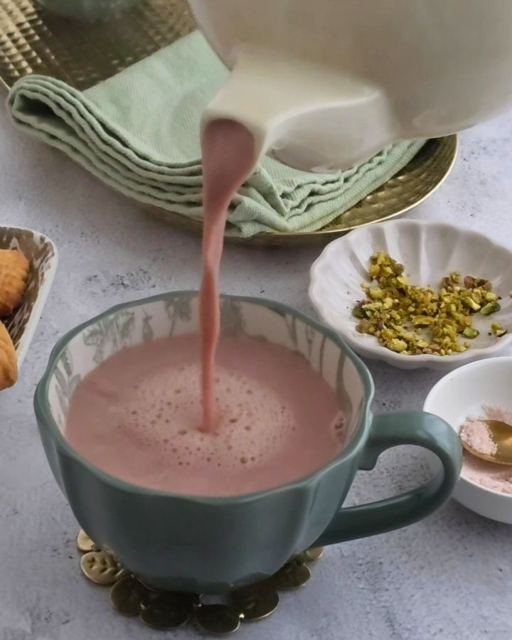Pouring Kashmiri Chai (Pink Tea) from teapot into cup, pink stream mid-pour