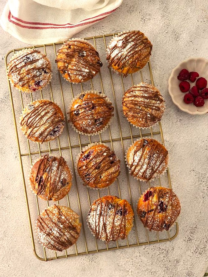 Muffins cooling on a wire rack, drizzled with melted chocolate and dusted with icing sugar.