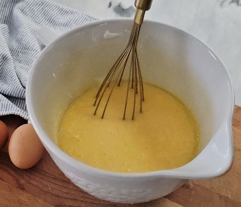 Whisking eggs, sugar, milk, and butter together in a mixing bowl for muffin batter.